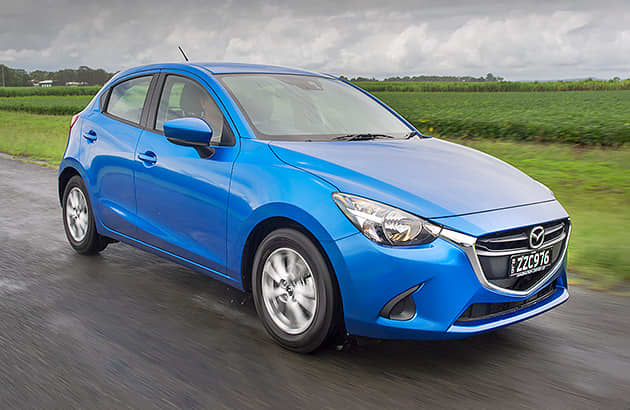 A blue Mazda2 driving on a country road.