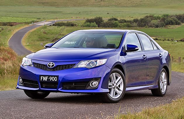 A blue Toyota Camry driving on a winding country road.