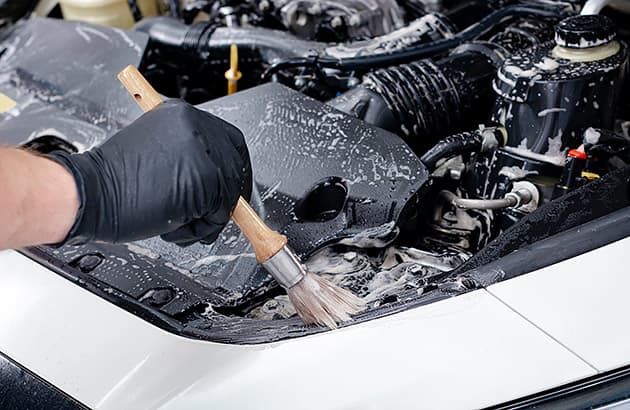 A close-up of someone cleaning residue off a car engine with a small brush