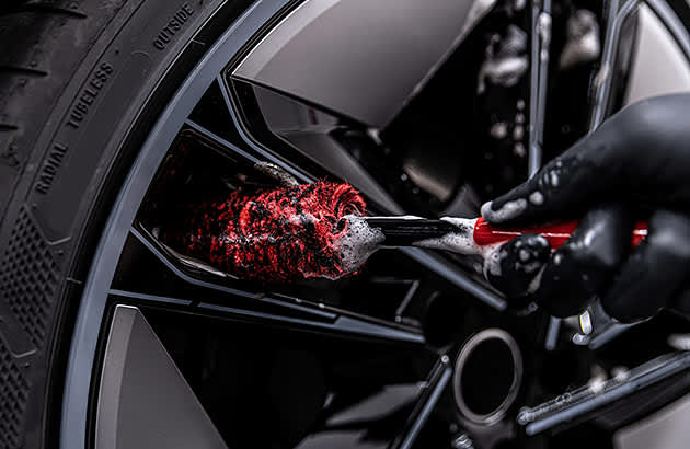 A close-up of someone scrubbing a car wheel with a brush