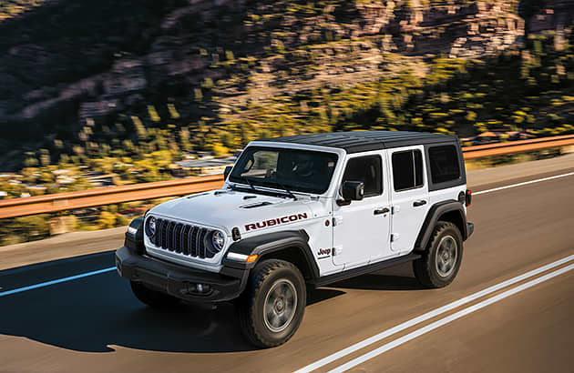 A white Jeep Wrangler on a winding country road