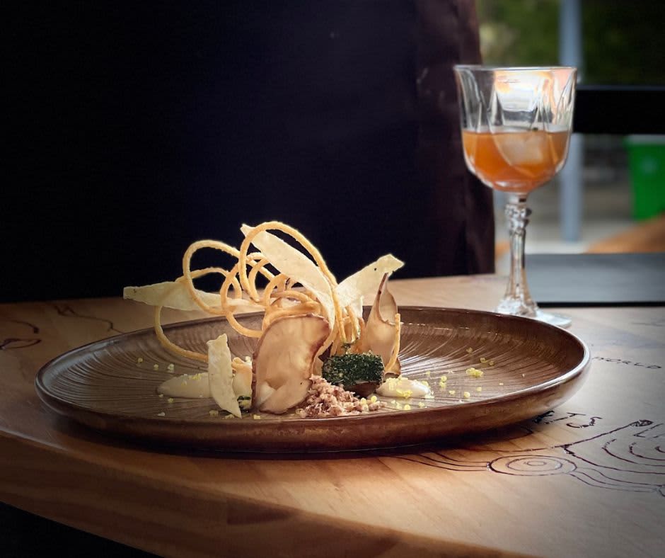 One of the Flackyard dishes on the menu on a brown plate with a glass of orange non-alcoholic wine with ice