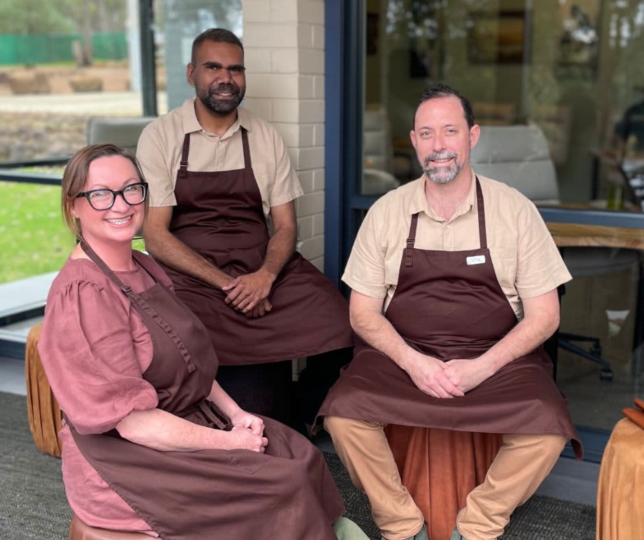 Owners Nik and Em Flack and Chef Dan seated outside in matching maroon aprons