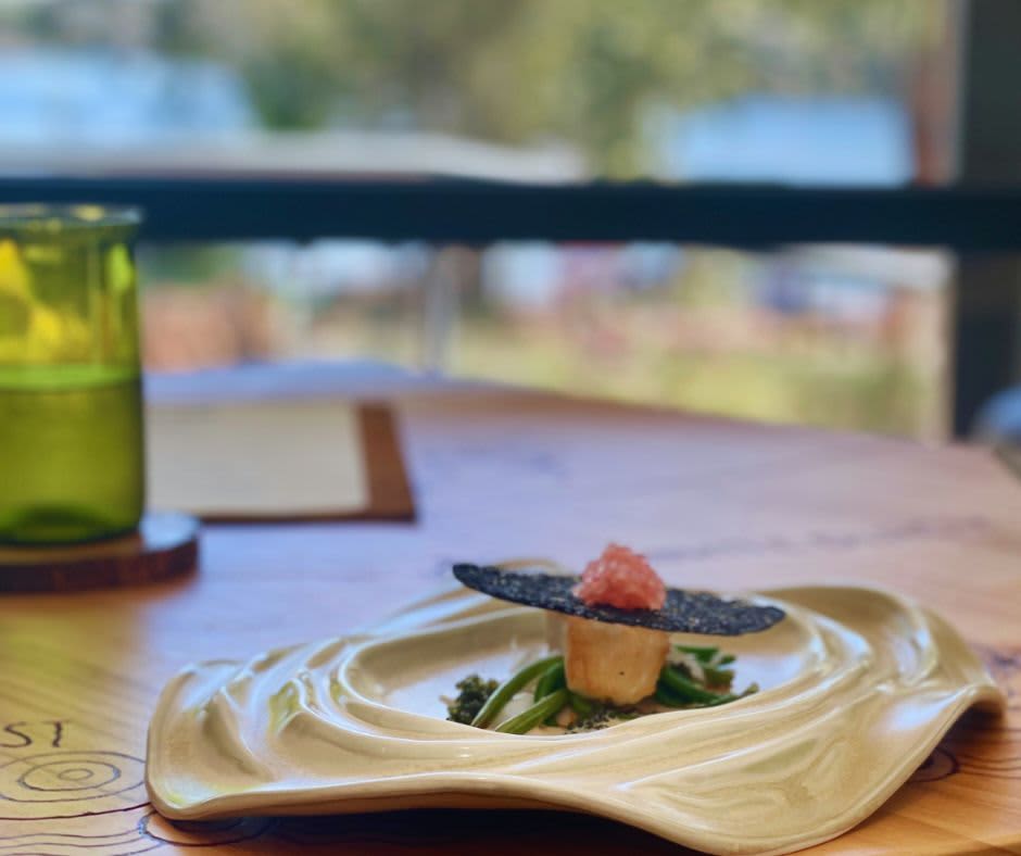A plate with fish and native ingredients on a table overlooking a lake in the background