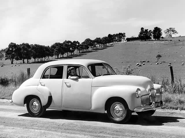 A 1948 Holden FX driving past paddocks