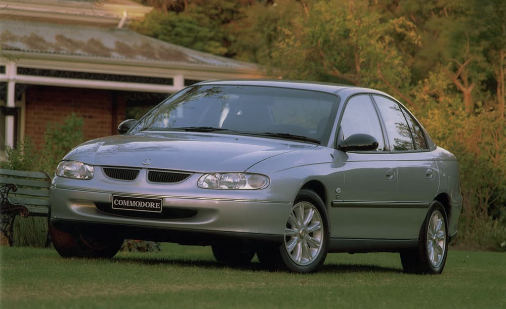 A grey Holden VT Commodore on a lawn outside a farmhouse