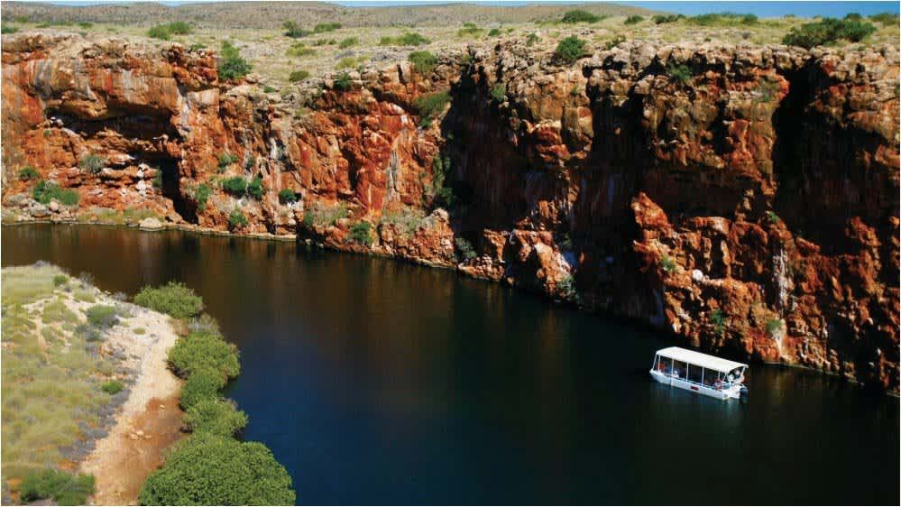 A tour boat on the dark waters of Yardie Creek with the gorge wall in the background.