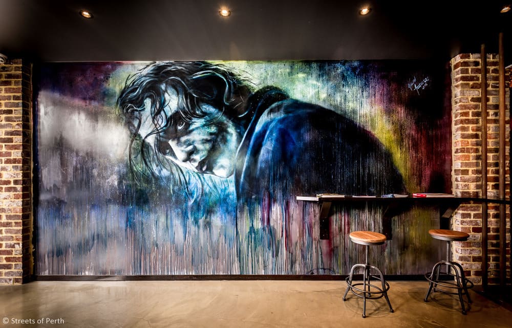 A large, stylised wall mural depicting the Joker character with chaotic, messy hair, looking over his shoulder.