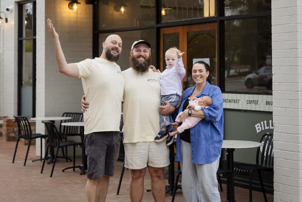 A family and two staff members stand outside a local cafe smiling for a photo.