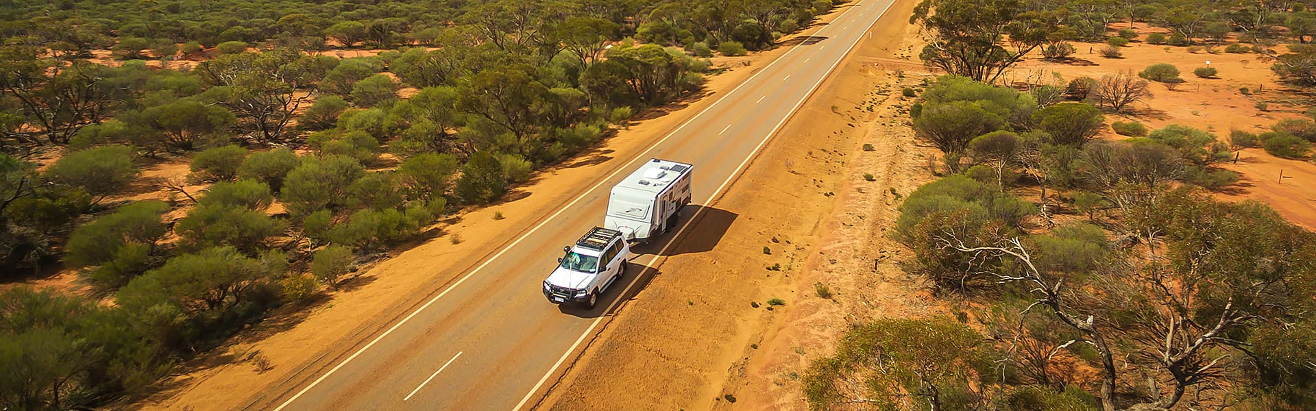 A car towing a caravan on a red dirt road