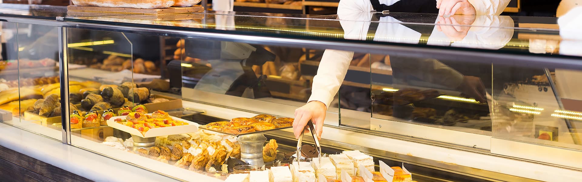 A bakery display cabinet with someone reaching in with tongs to get a cake