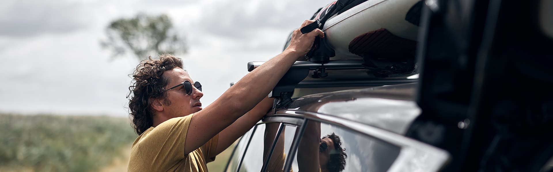 A man is checking the strapping on his loaded roof rack