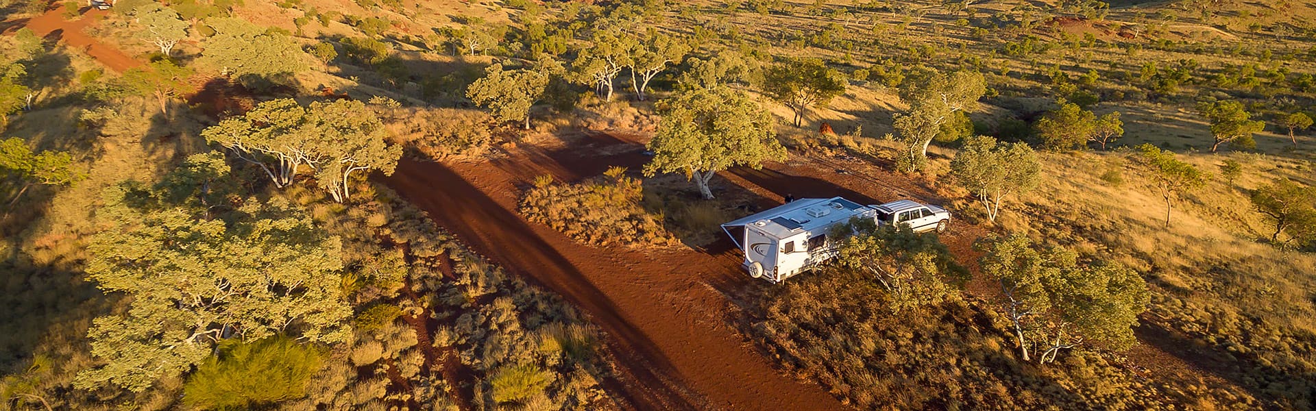 An aerial image of a four-wheel drive and caravan parked in a clearing off a red dirt road