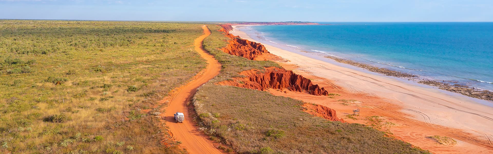 A car on a red dirt track near the ocean near Broome