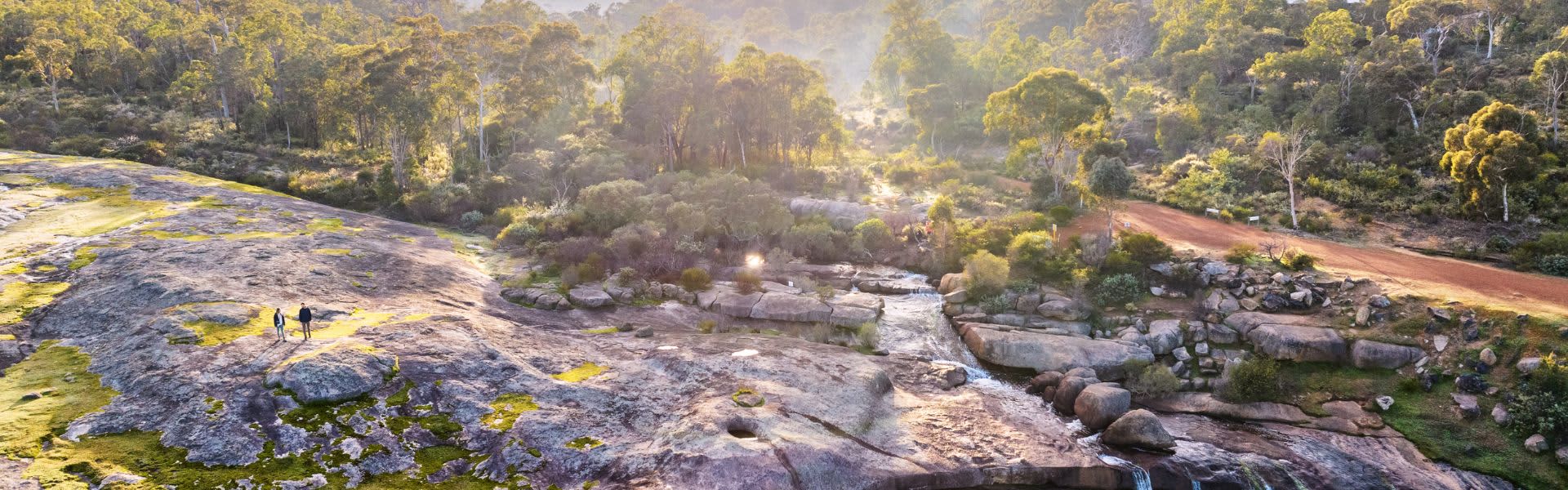 two people hiking in hills next to flowing waterfall