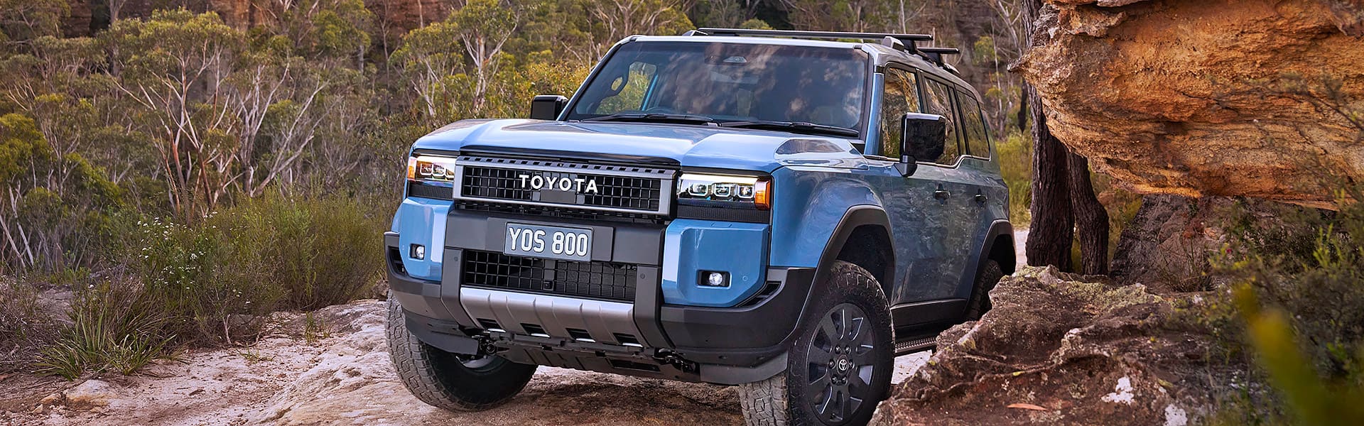 A blue Toyota Prado driving through a rocky landscape