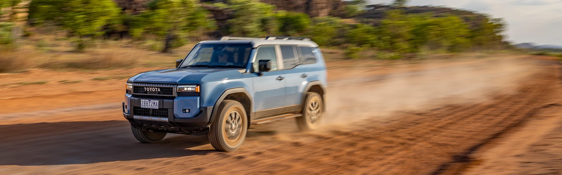 A blue Toyota Prado driving along an outback gravel road