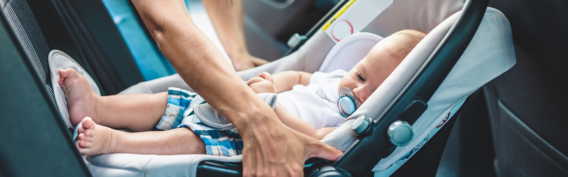 A rear facing child seat being handled by a parent in a car