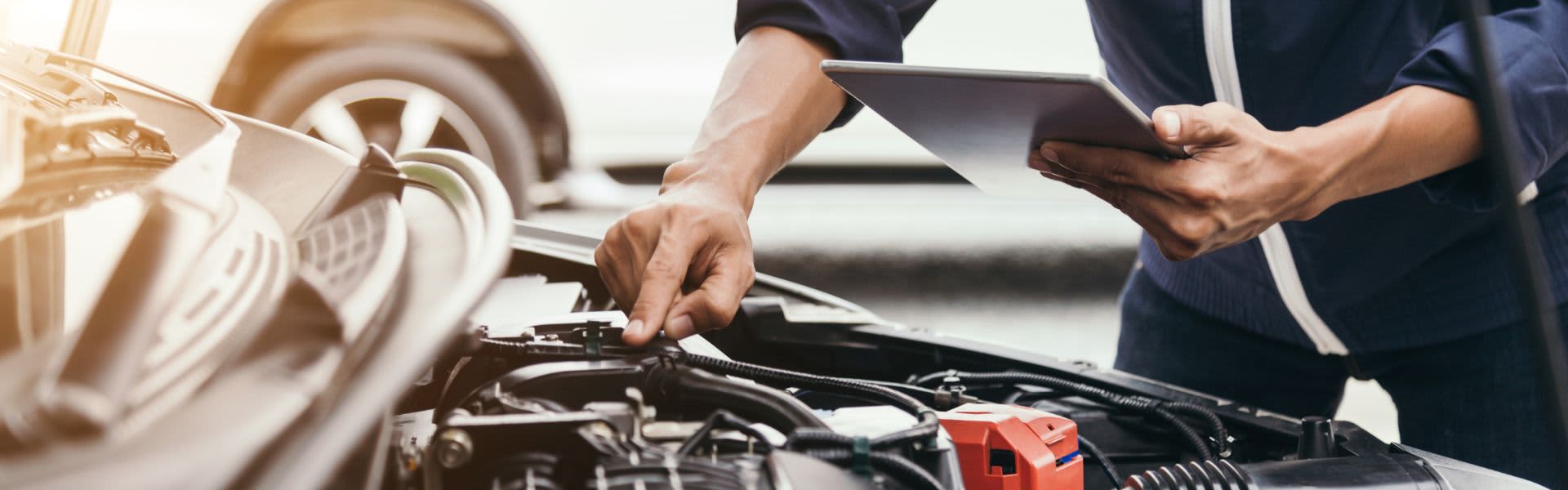 Man with hood of car open holding tablet inspecting car
