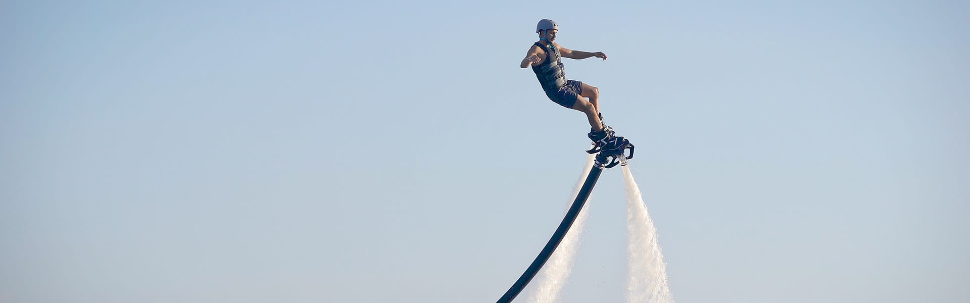 A man is airborne riding a flyboard device with waterjets shooting downwards