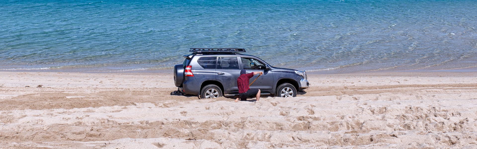 Man digging out sand from around bogged vehicle