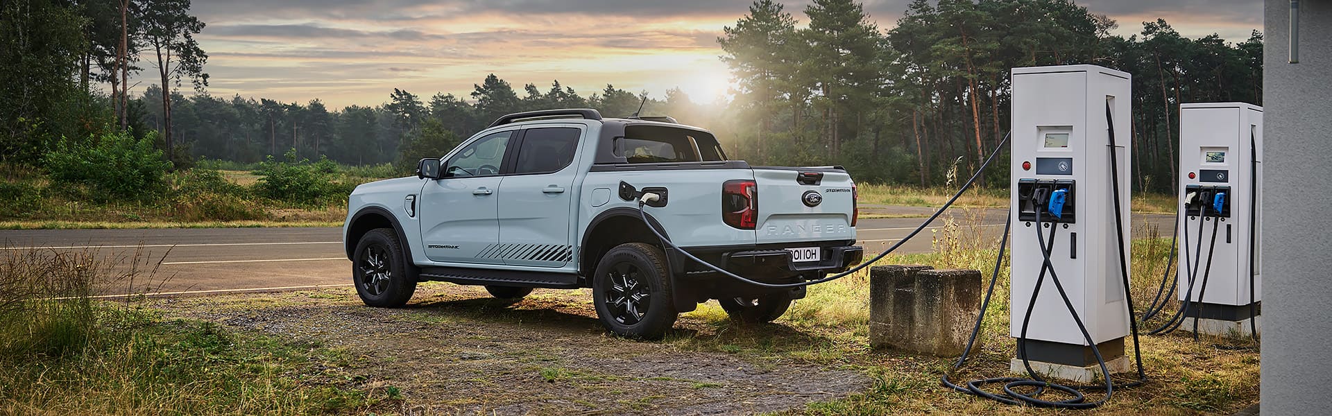 A white Ford Ranger EV parked at a charger in a country landscape