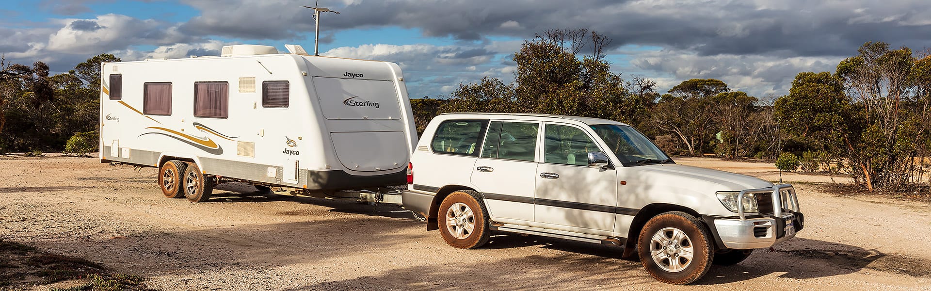 A white four-wheel drive pulling a large dual-axle caravan along a dirt track