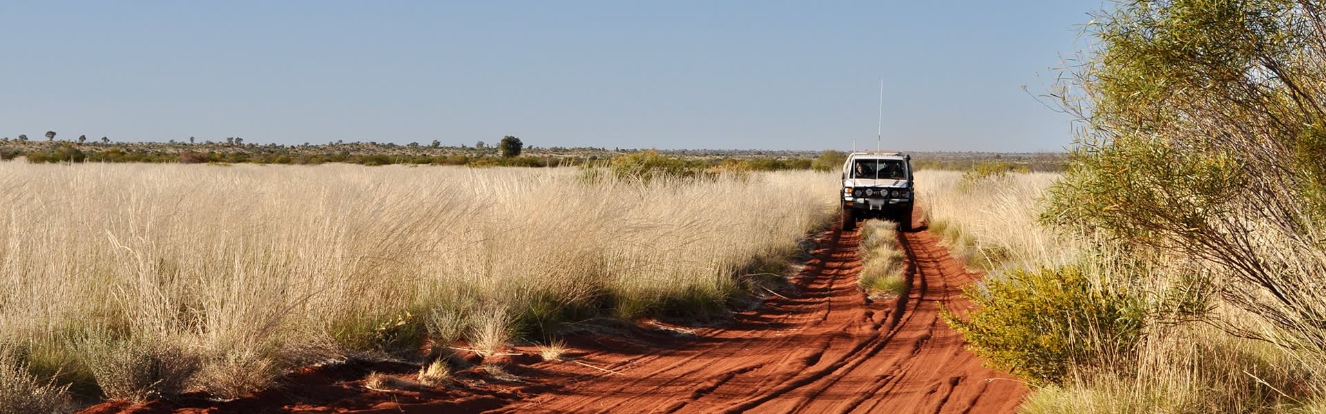 White four-wheel drive, driving on red dirt road in Australian outback.