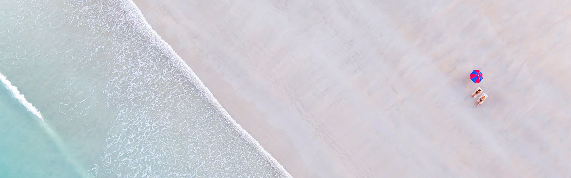 Two people lying under an umbrella on Cable Beach in Broome