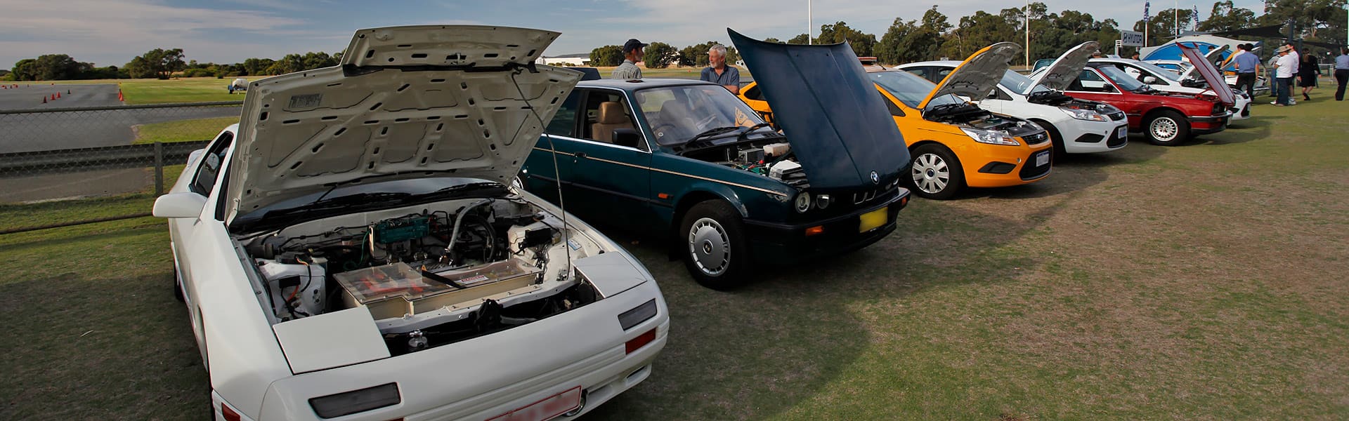 A row of older cars with bonnets up showing EV motors and battery packs