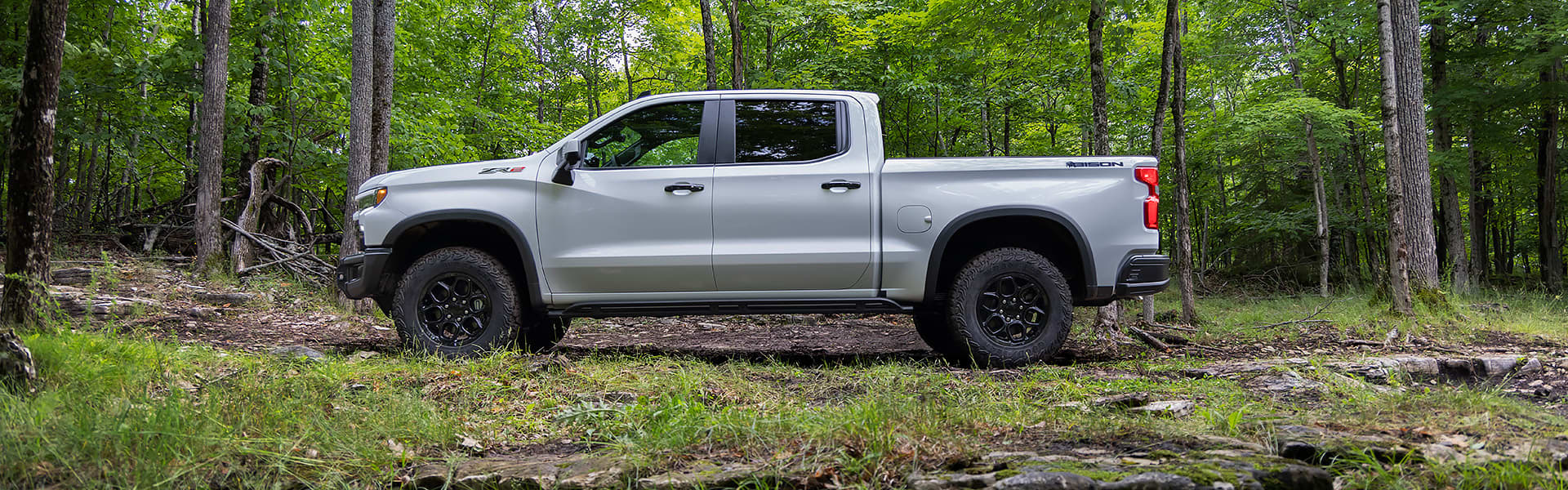 A white Chevrolet Silverado parked in a forest seen from the side