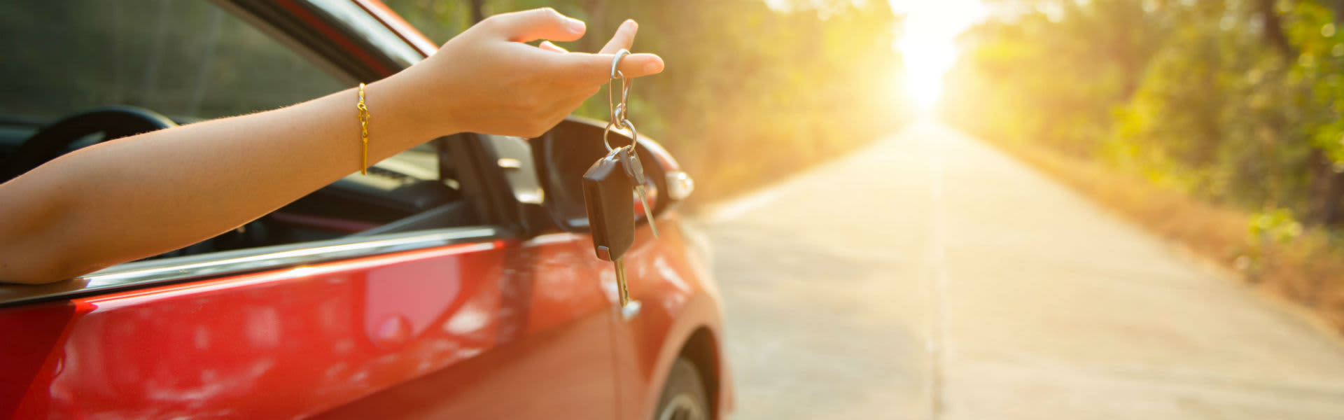 A woman holding her car keys out of the window of her parked car