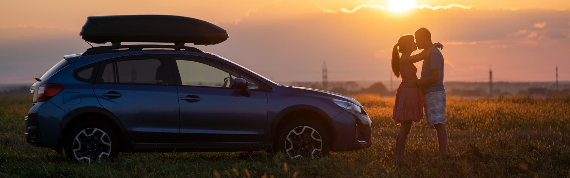 Couple in a field embracing at sunset next to their car