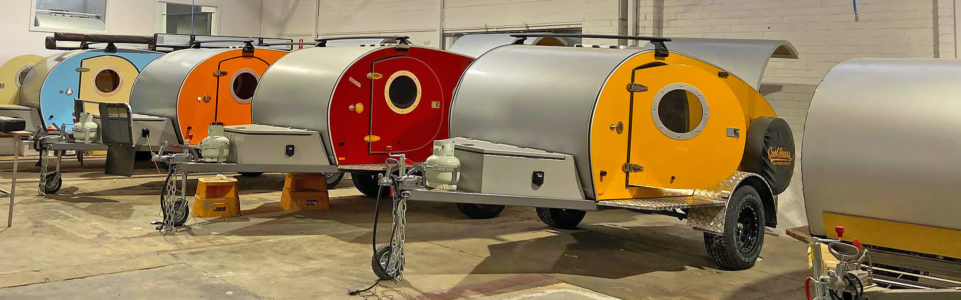 A row of teardrop campers in various colours in a factory setting
