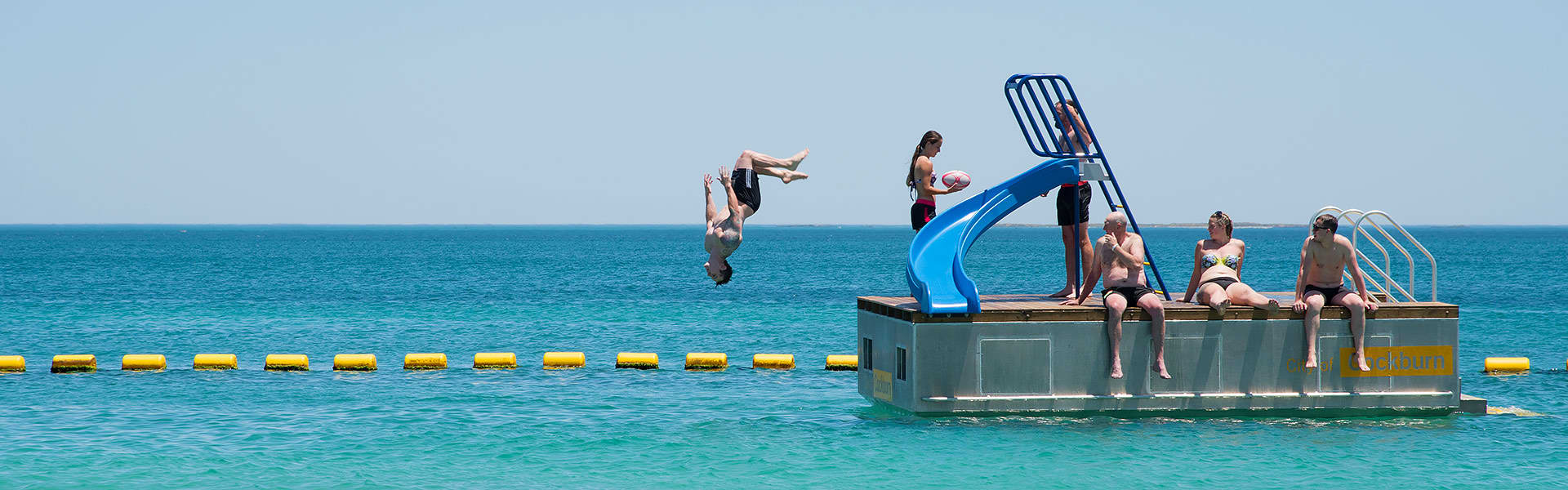 Kids swimming at the beach and one jumping from a pontoon