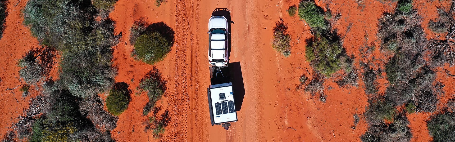 An aerial shot of a car and caravan travelling down a red dirt road