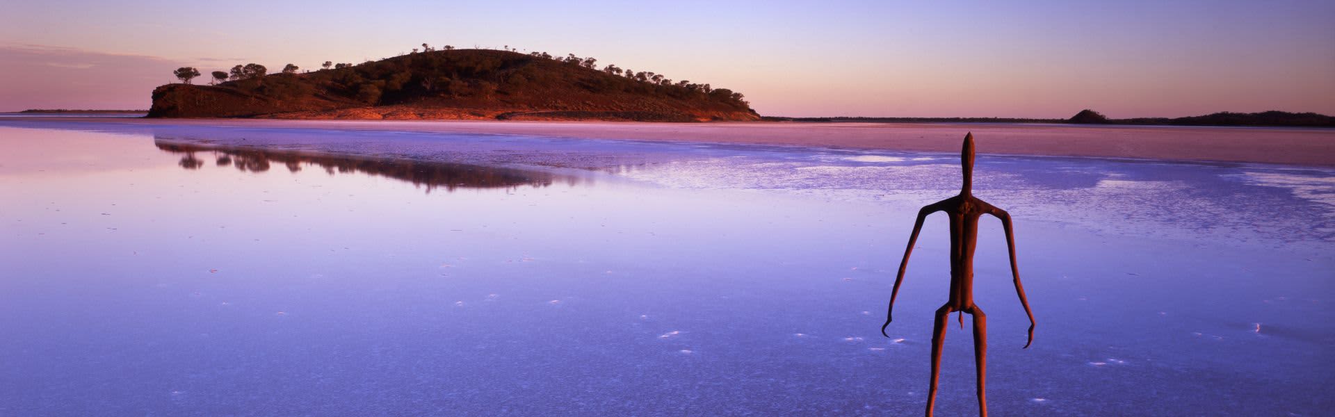 sculpture of a man standing in lake looking at island at sunset