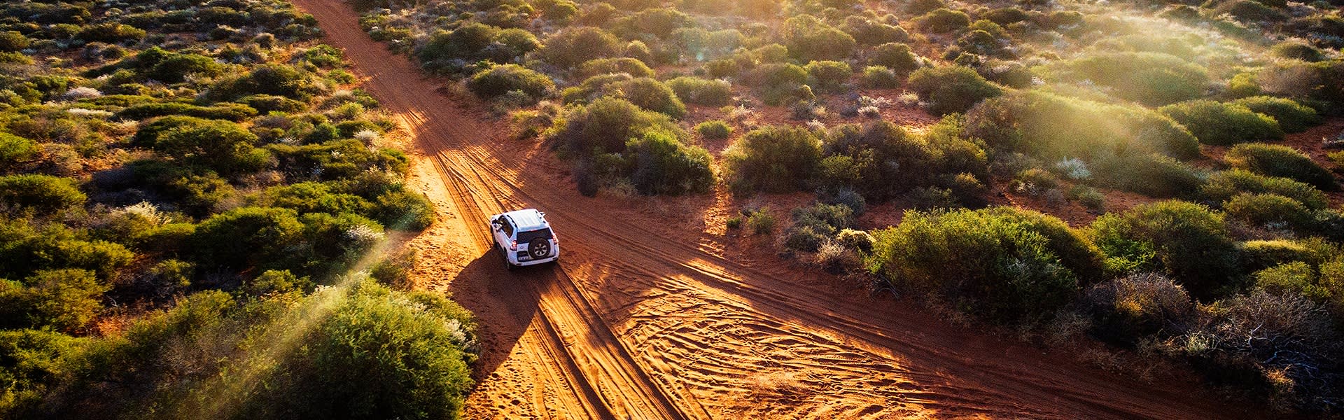 White car driving on red dirt road through Australian outback