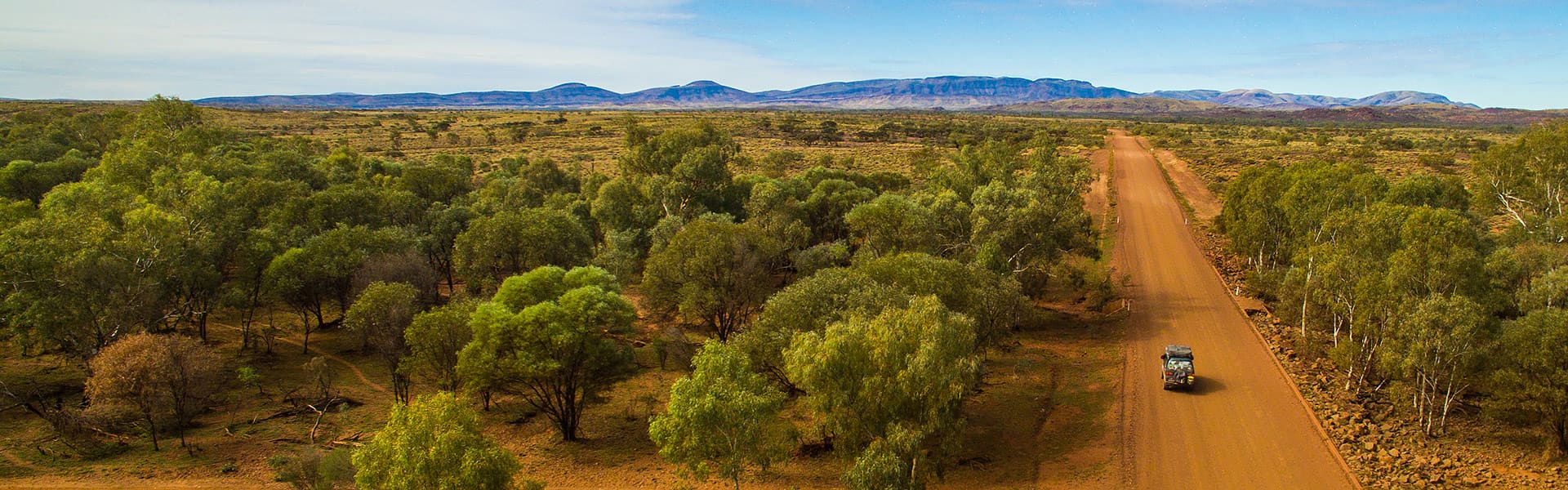 An aerial image of a car travelling down red dirt road