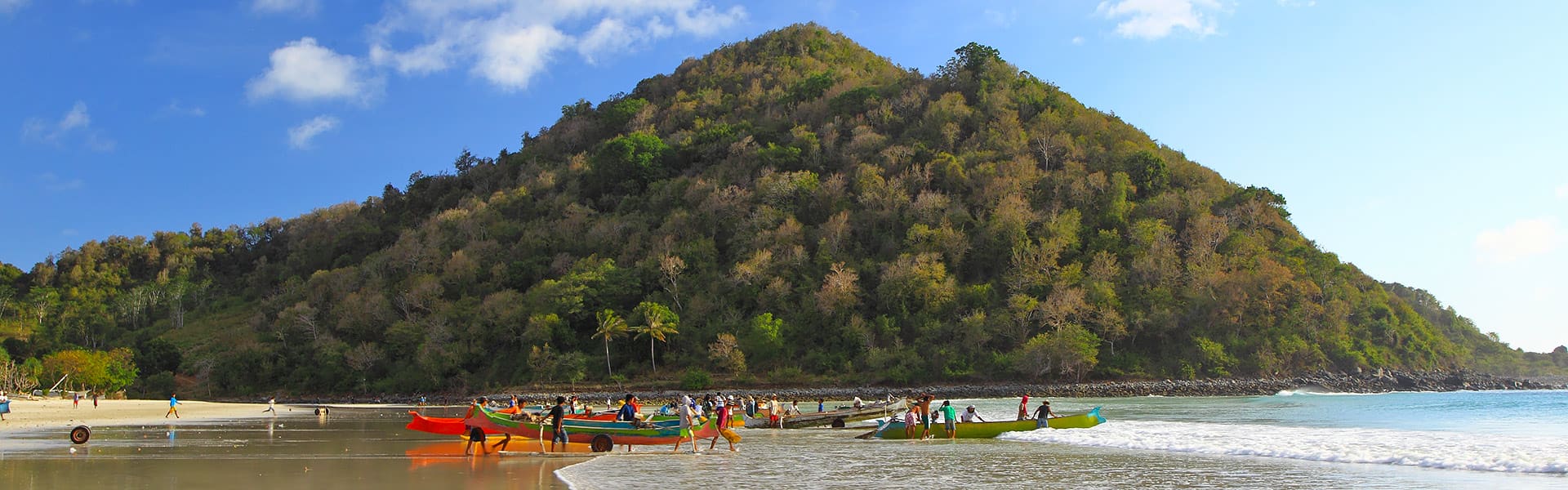 A tropical beach with boats on shore and a hill in the distance