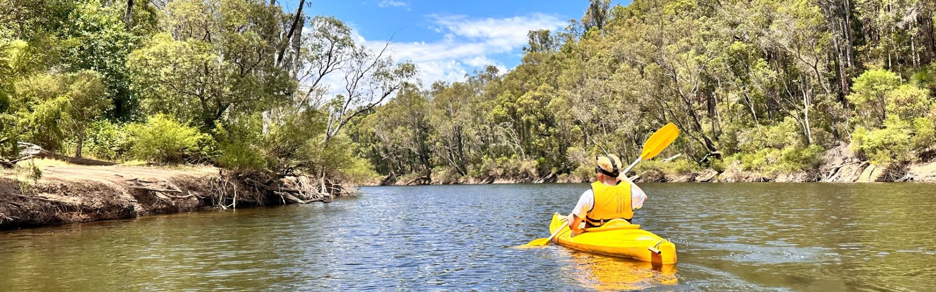Person paddling down river in yellow kayak