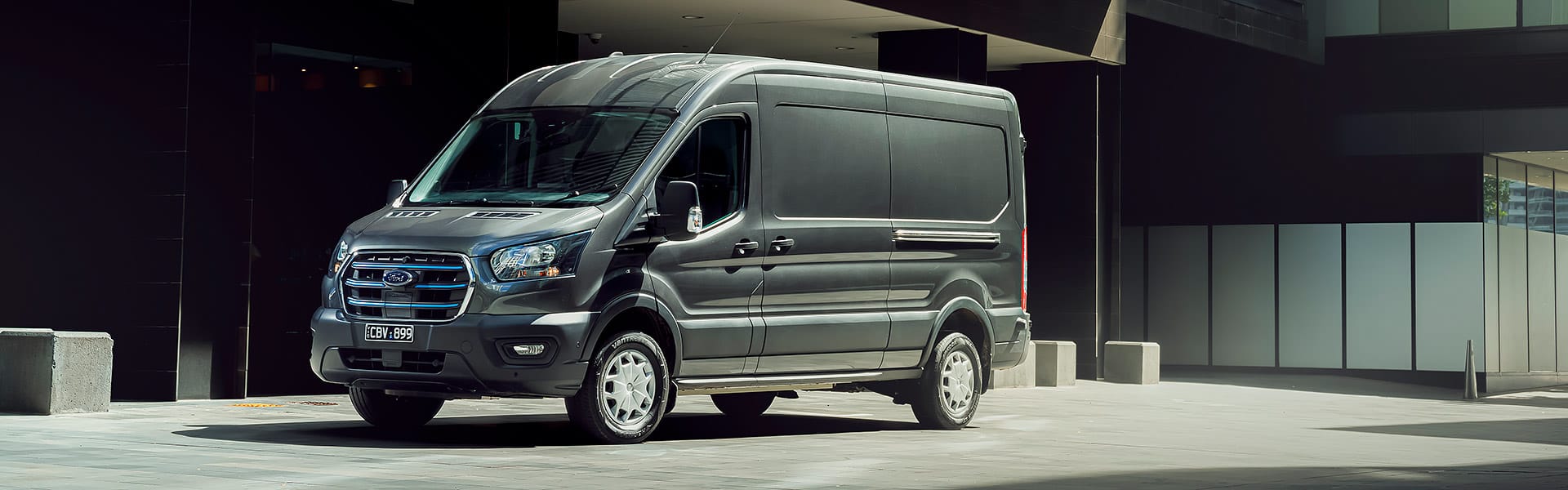 A grey Ford e-Transit van parked outside a city building