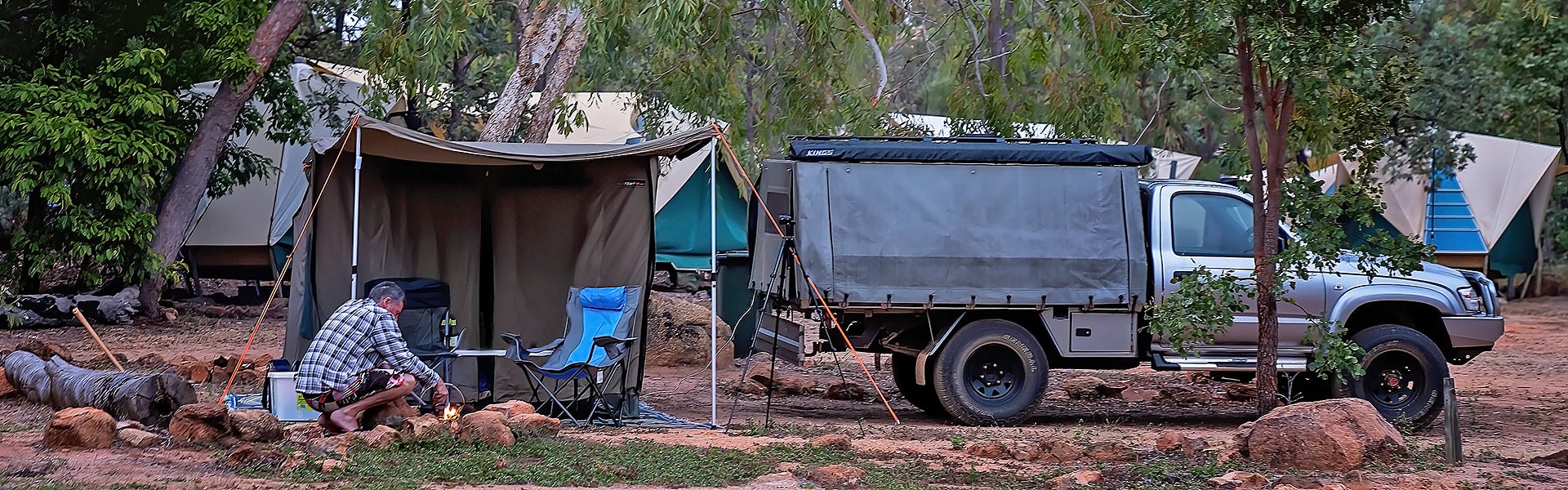 A man tending a campfire near an awning in a caravan park