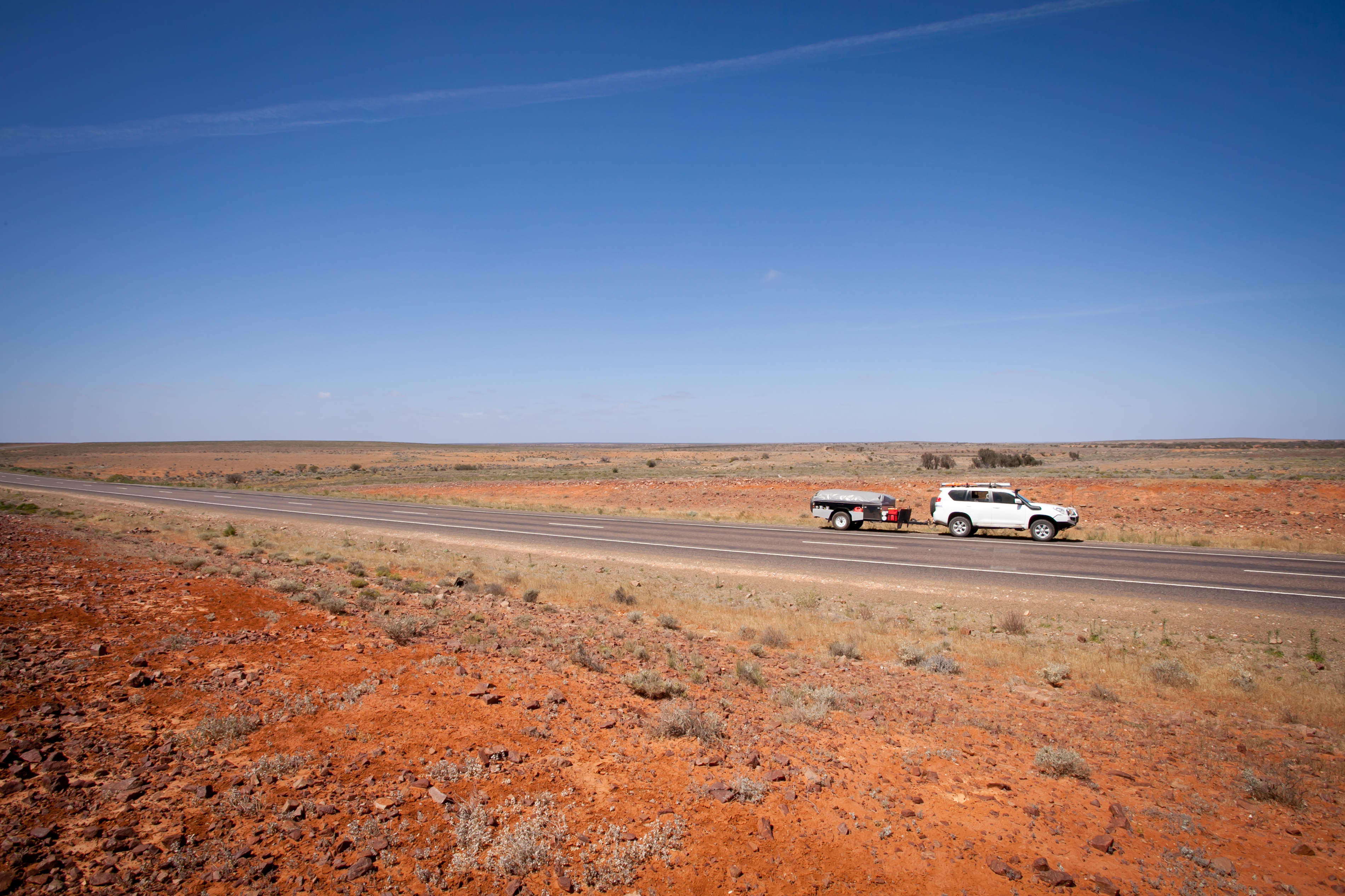 A car on an outback road towing a small trailer