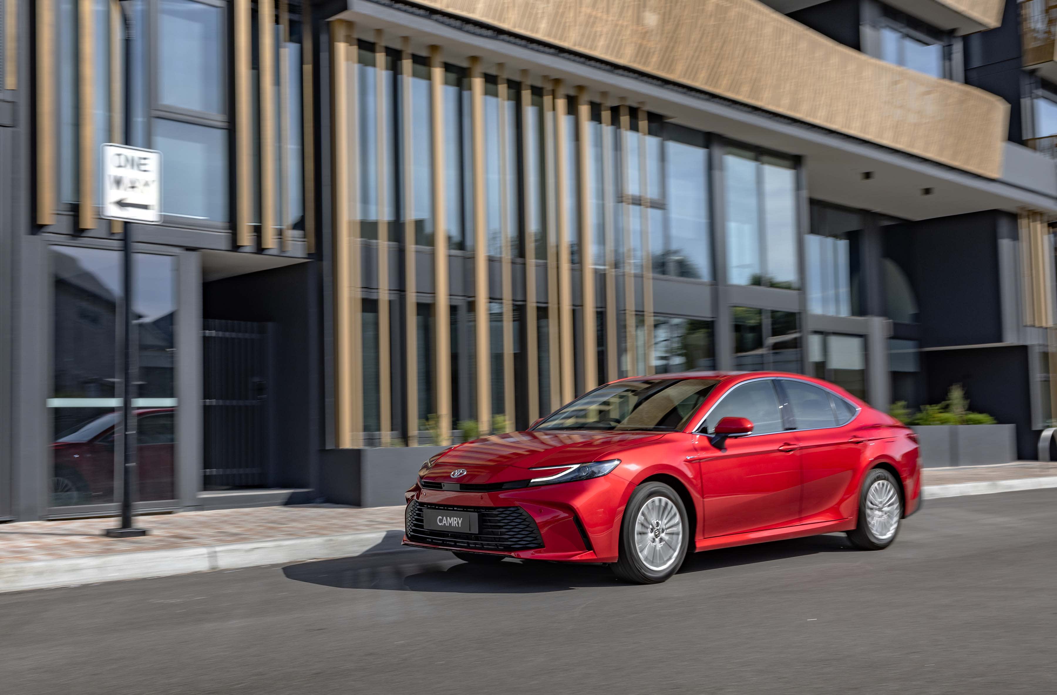 A red Toyota Camry parked outside a city building