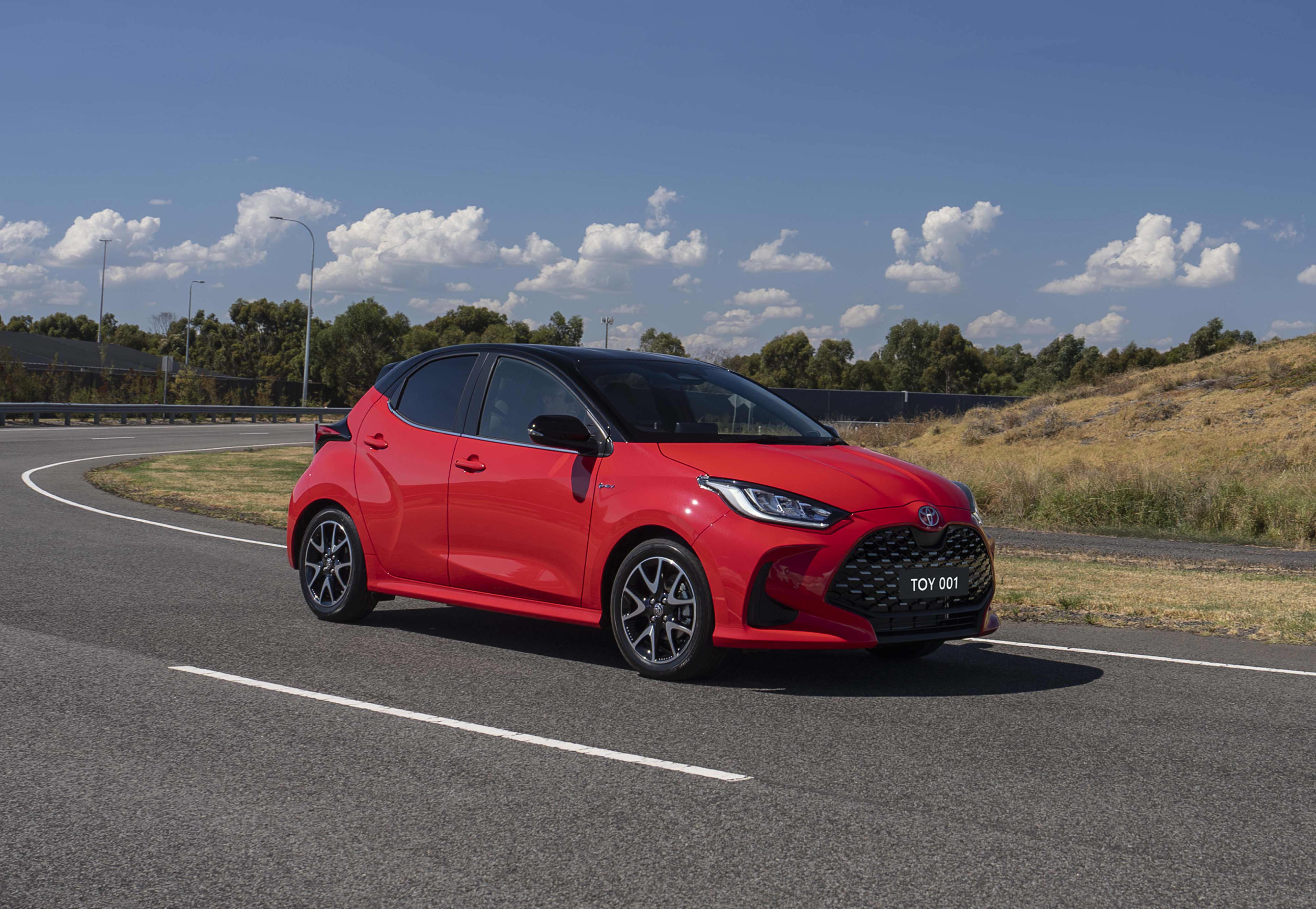 A red Toyota Yaris driving on a country road