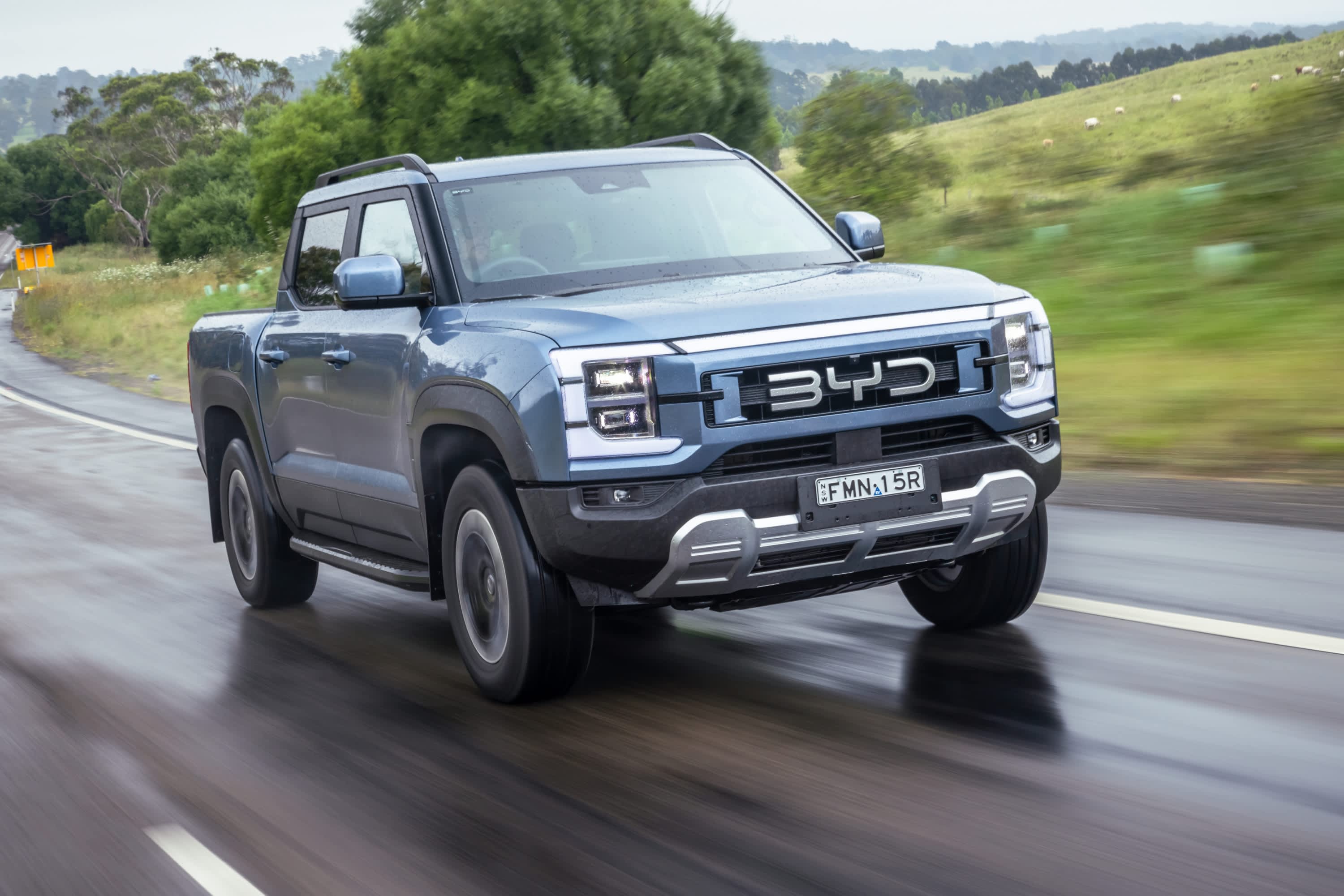 A blue BYD ute driving on a wet country road