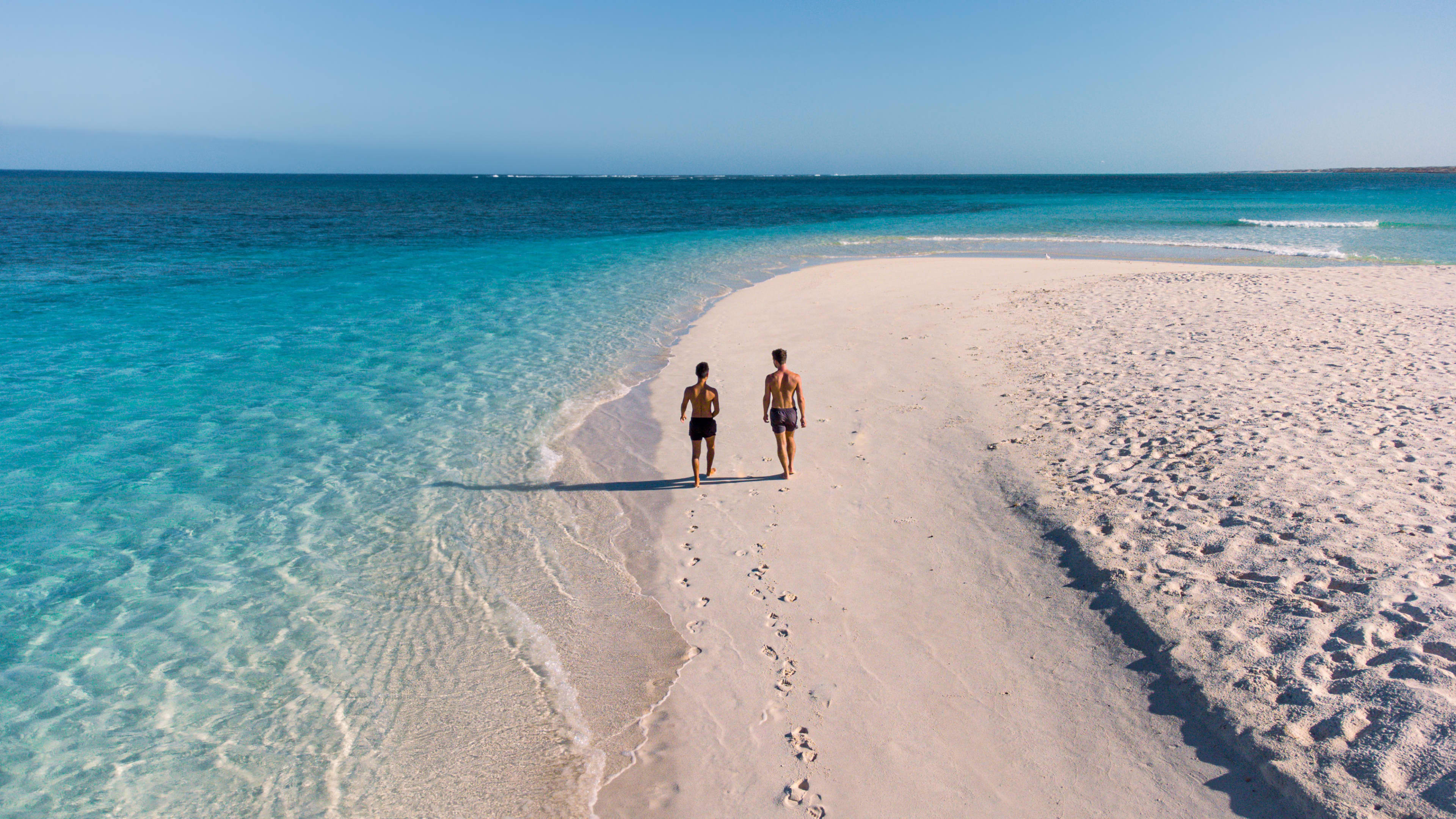 Two people walking along a white-sand beach in Exmouth