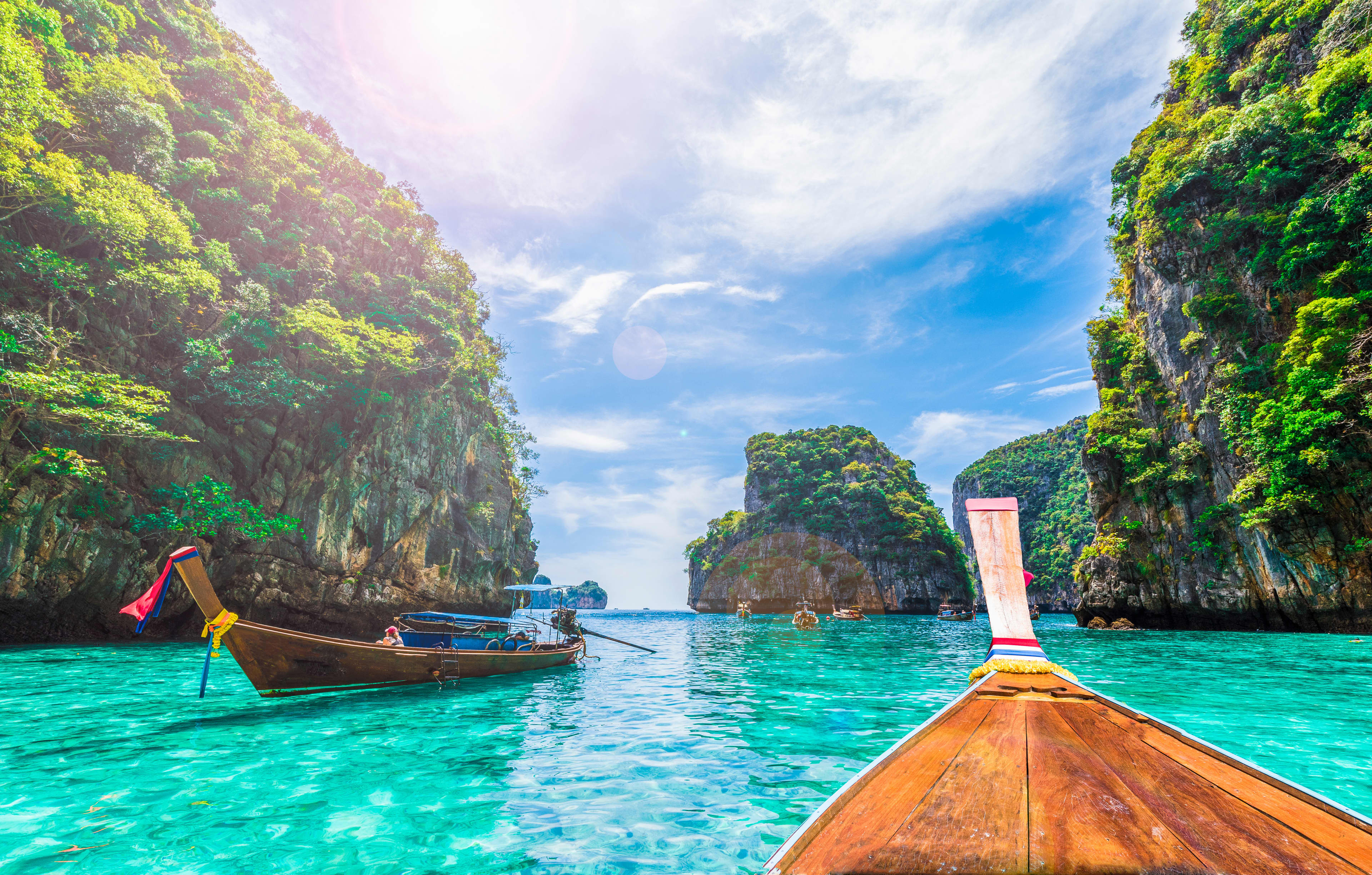 Boats floating on turquoise waters surrounded by tree-covered rocks at Phi Phi island