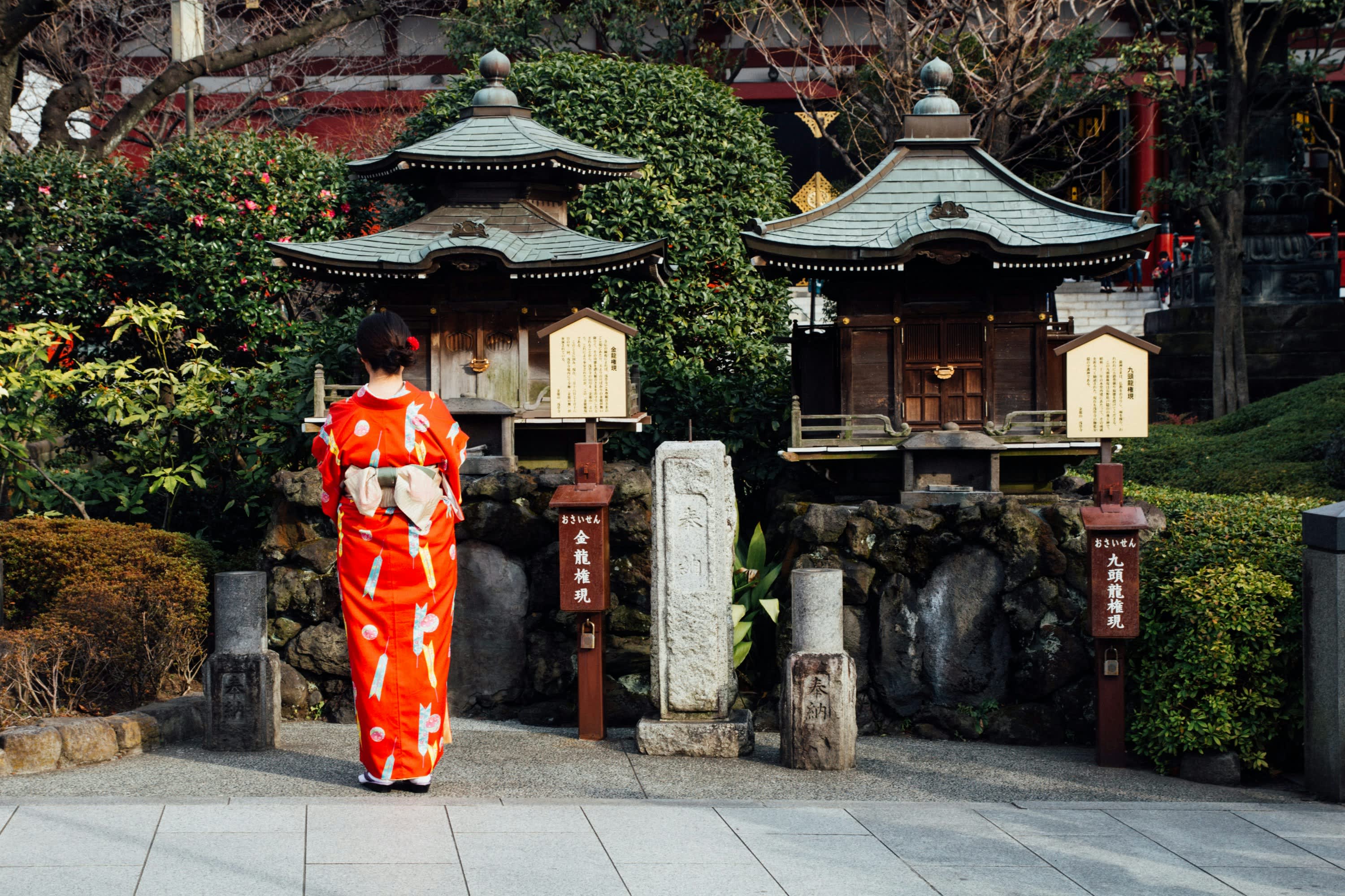 Woman in red kimono in front of two small shrines